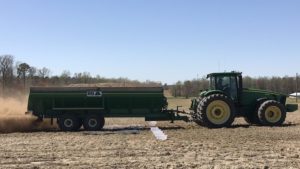 John Deere tracker pulling a litter spreader across a field