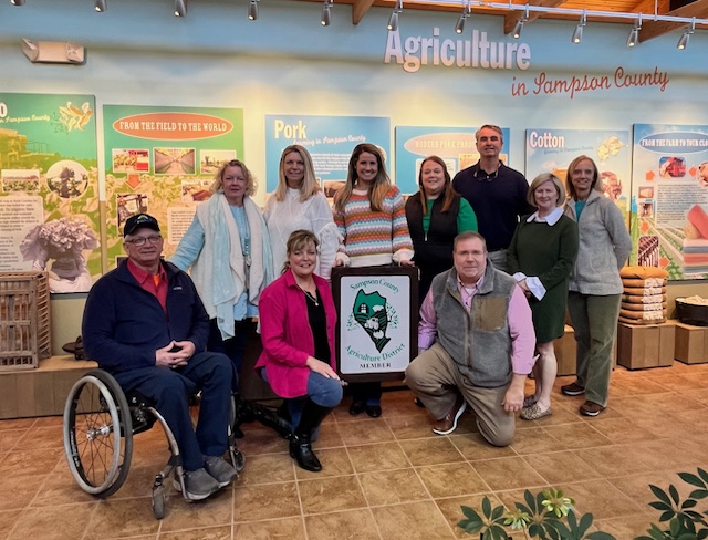 Sampson Ag Advisory Board with new farm sign (2024): Kent Fann, Jennifer Daniels, Nelson Powell (front row); Wendy Dorman, Anita Lane, Morgan Moore, Melanie Harris, Henry Faison, Susan Heath, Eileen Coite (back row)